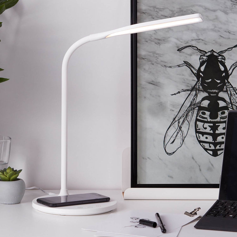 Lampe posée sur un bureau, smartphone en recharge sans fil devant une affiche encadrée