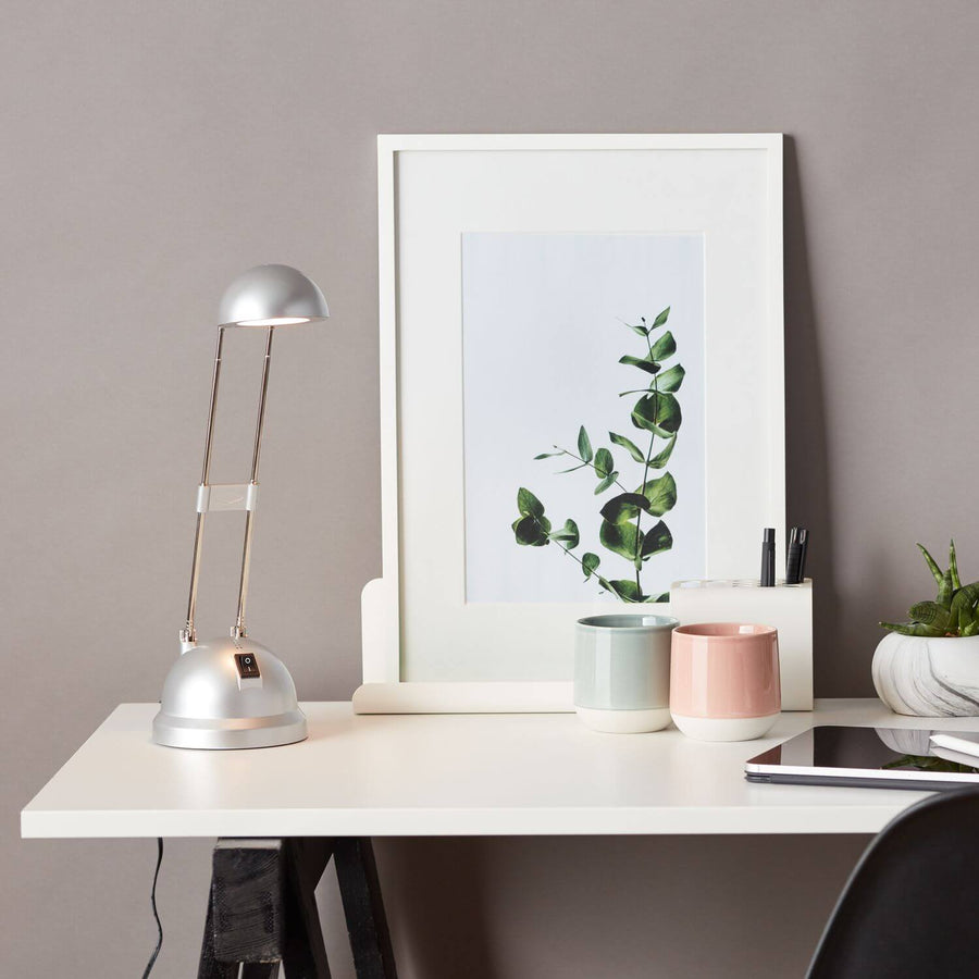 Vue d'ensemble du bureau avec la lampe allumée, un cadre, des tasses et une tablette.
