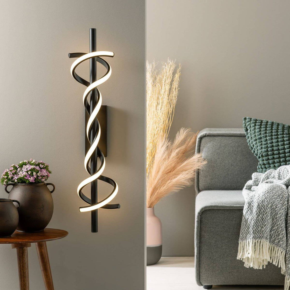 Applique murale verticale noire avec spirale lumineuse, posée sur un mur beige.