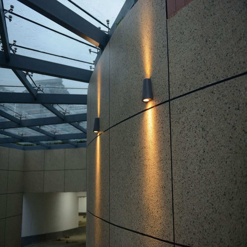 Deux appliques noires éclairant un mur de béton sous une verrière extérieure