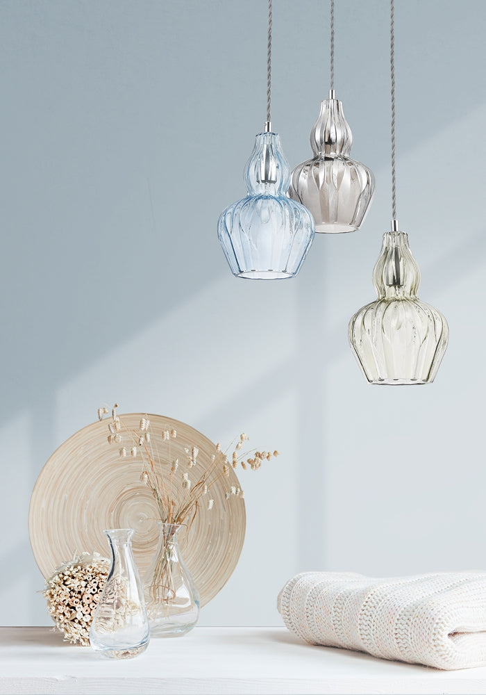 Mise en ambiance avec trois suspensions coloris bleu, transparent et fumé, décor naturel et textile.