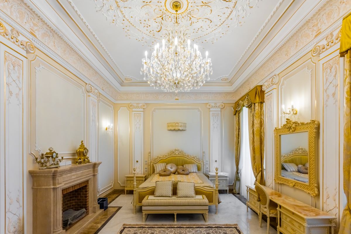 Lustre installé au centre d'une chambre classique dorée, lit et cheminée visibles