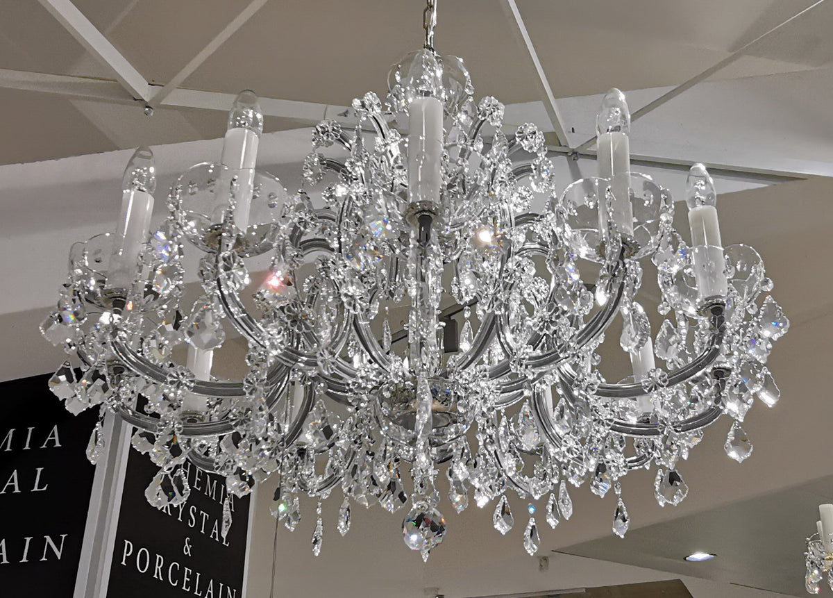 Vue rapprochée du lustre suspendu au plafond, montrant bras courbés et pendeloques taillées.