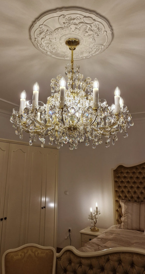 Détail du lustre sous une rosace de plafond ornée, cristaux et bougies allumées.