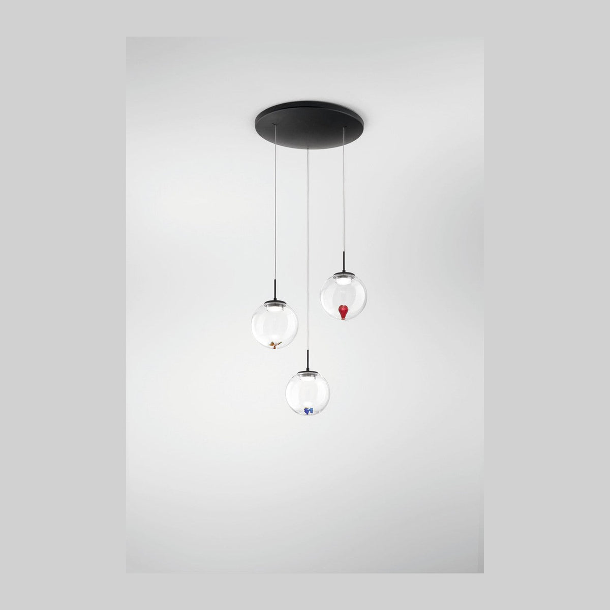 Vue de face d'une suspension à trois globes de verre transparent sur fond blanc.