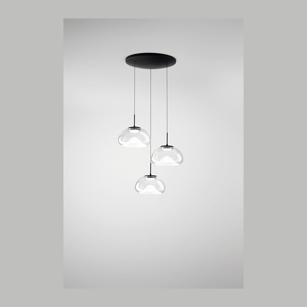 Vue de face de la suspension à trois globes transparents et câbles noirs, fond gris.