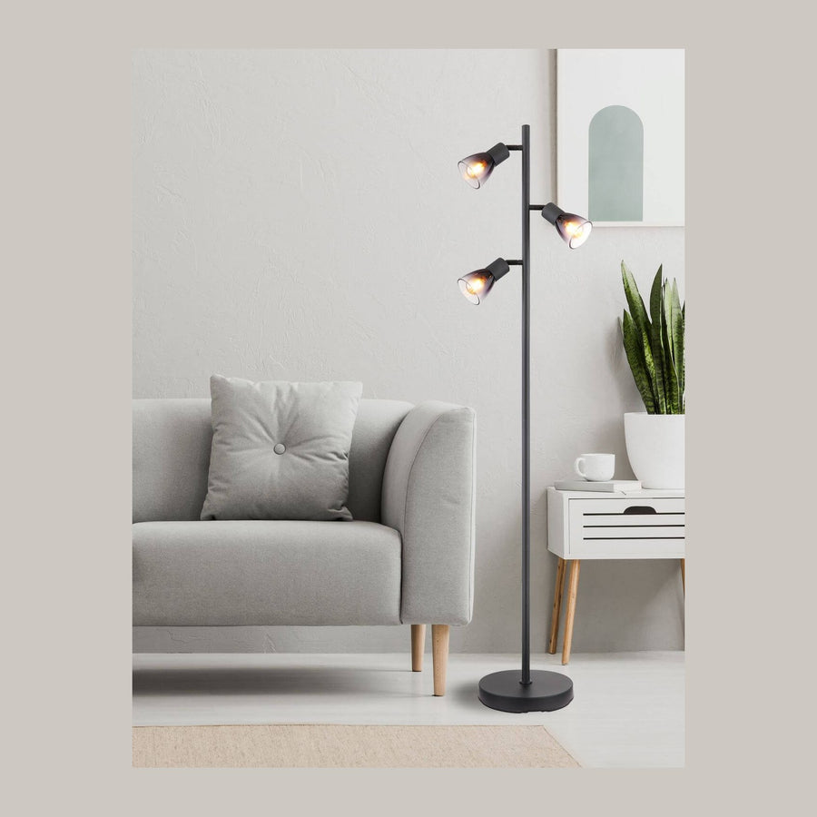 Lampadaire noir allumé dans un salon gris, près d'un canapé, d'un tableau et d'une plante