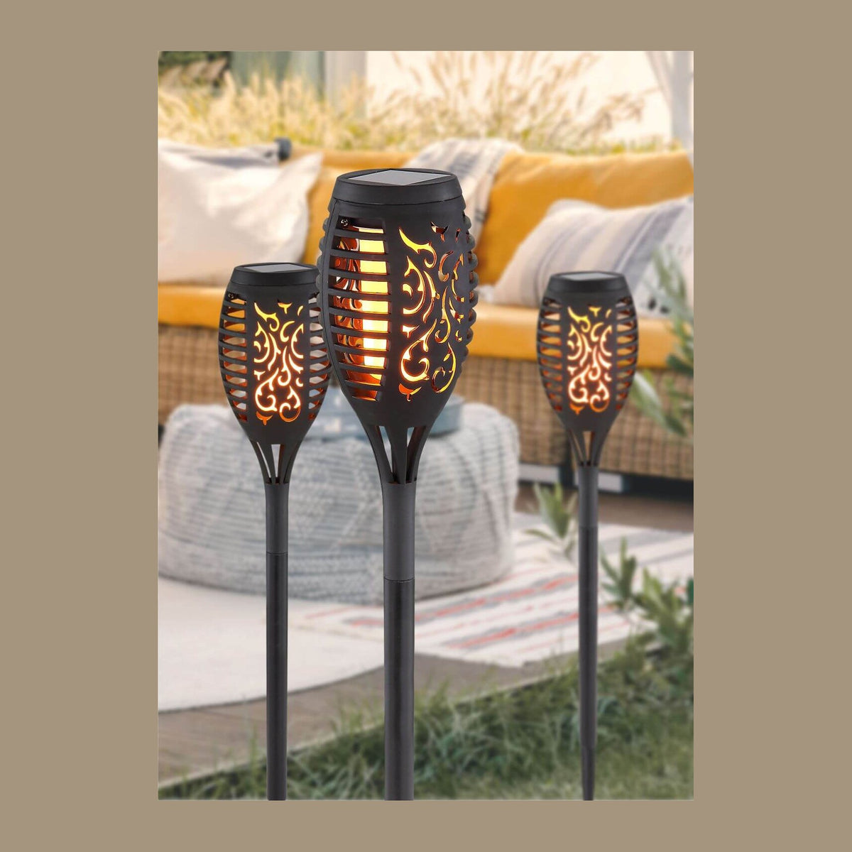 Trois torches solaires noires allumées plantées dans un jardin, canapé jaune flou.