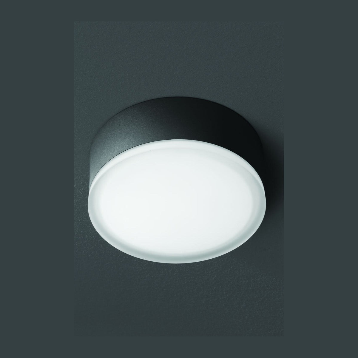 Vue de face du luminaire rond anthracite allumé sur fond gris sombre
