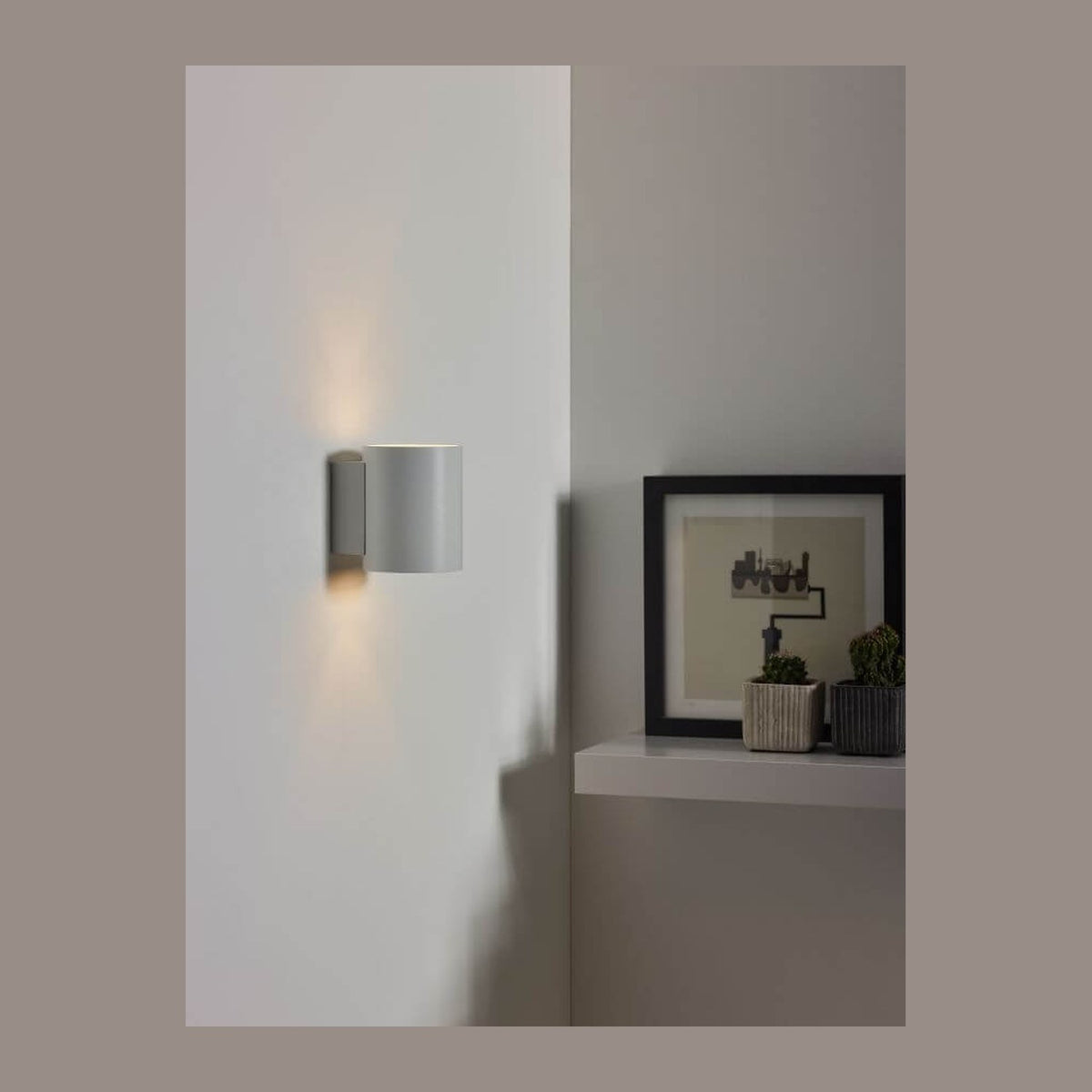 Applique murale blanche allumée sur un mur, effet lumineux haut et bas, ambiance intérieure.