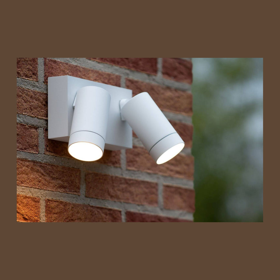 Applique blanche à deux spots cylindriques allumés sur un mur de briques rouges