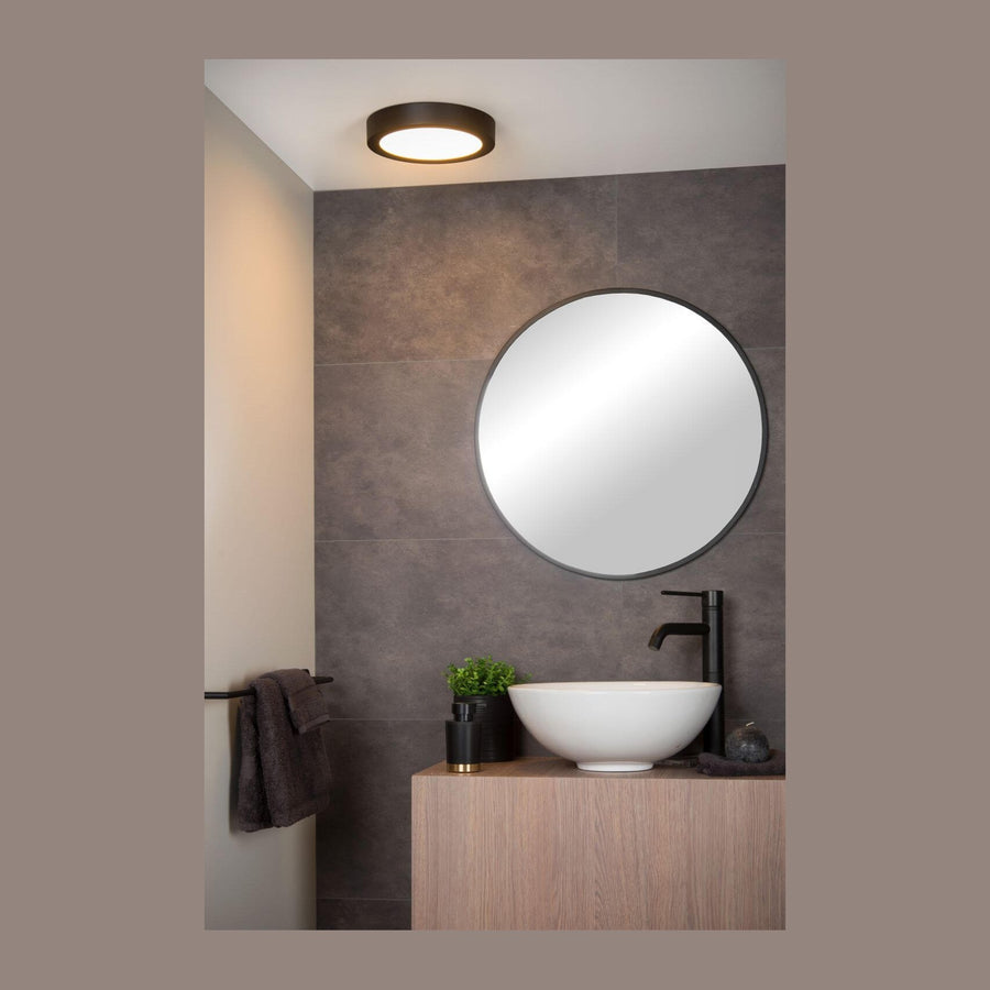 Plafonnier rond noir allumé au plafond dans une salle de bain moderne