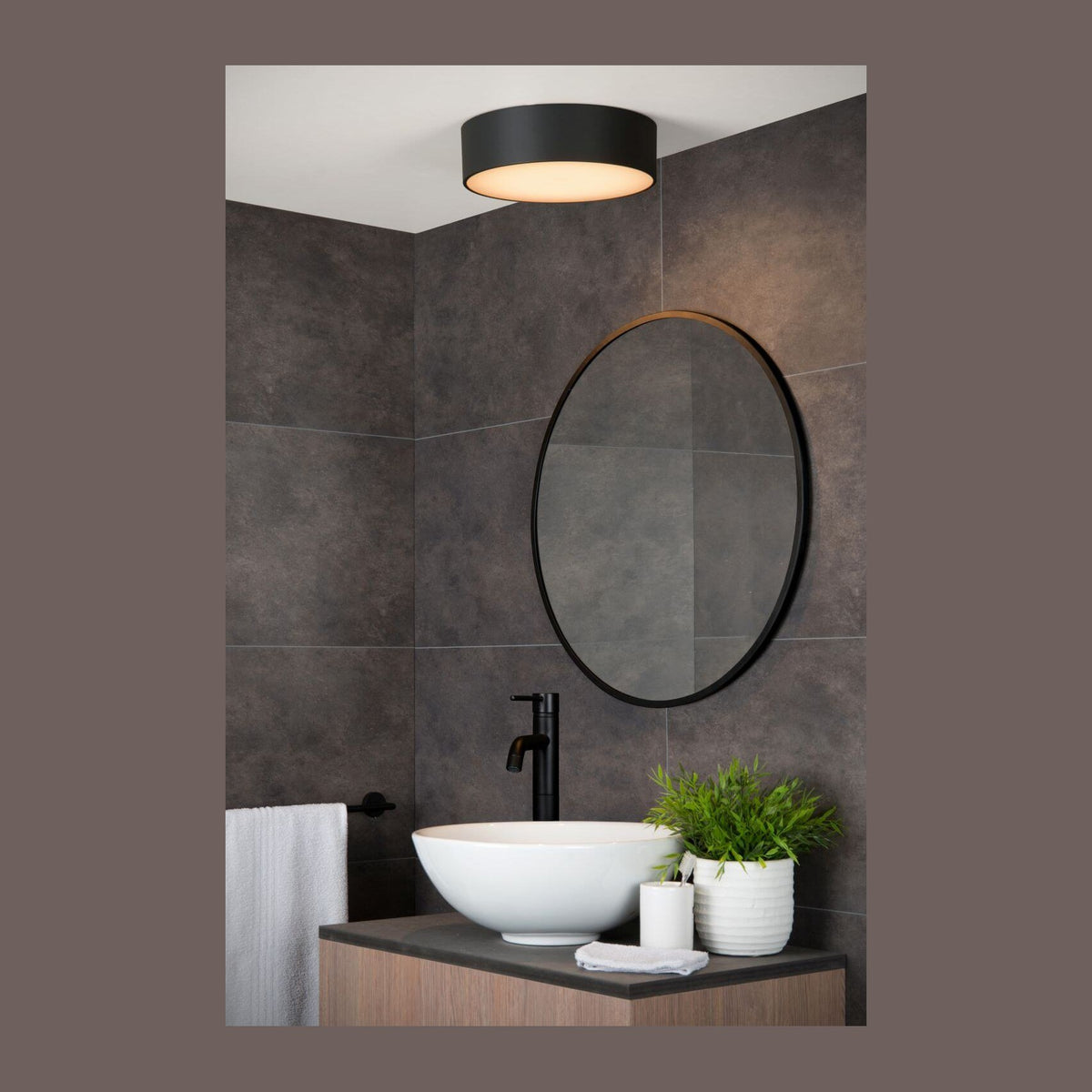 Mise en ambiance d'une salle de bain moderne avec plafonnier allumé au plafond au-dessus du lavabo.