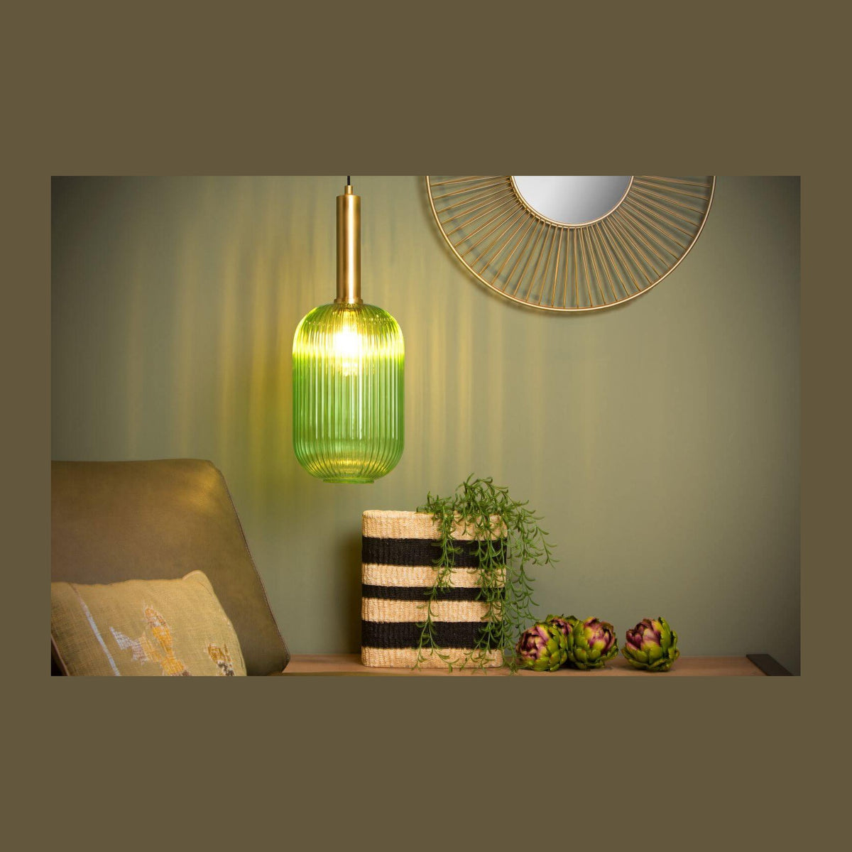 Suspension verte allumée dans un salon, fauteuil, miroir doré et panier tressé.