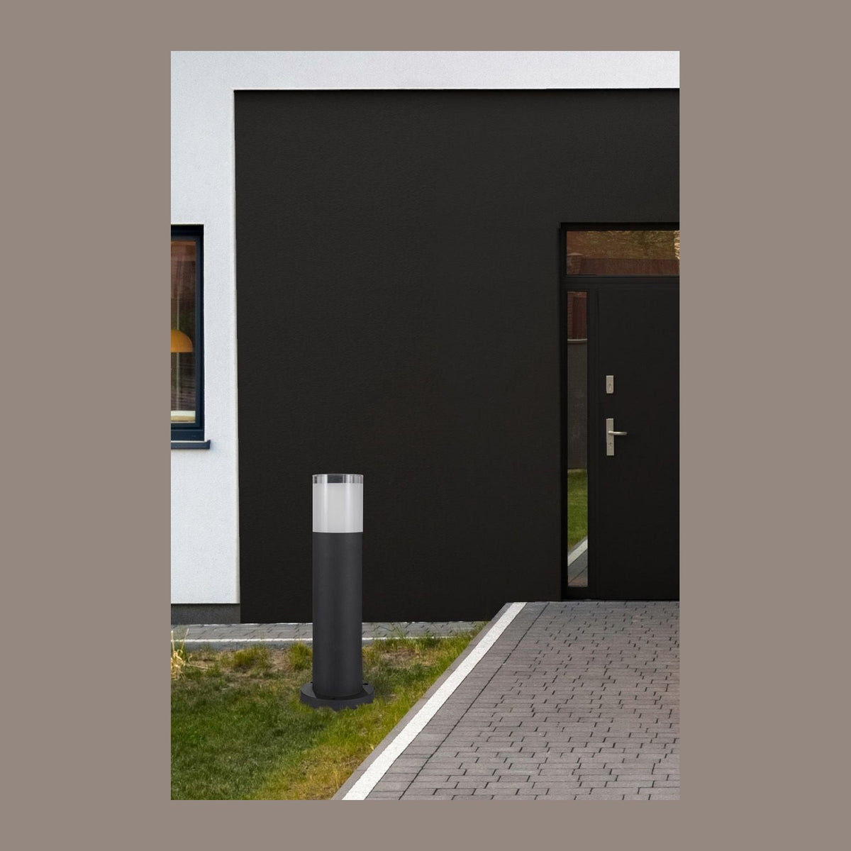 Borne noire installée dans une pelouse devant une façade sombre et une allée pavée.