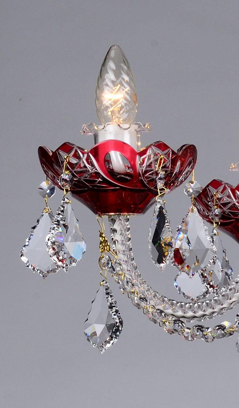 Gros plan sur une bobèche rouge ciselée, pendentifs de cristal et ampoule transparente allumée.
