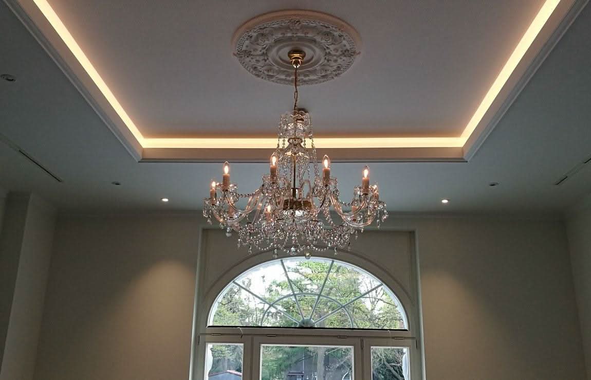 Vue en contre-plongée du lustre installé, allumé, sous un plafond avec éclairage indirect.