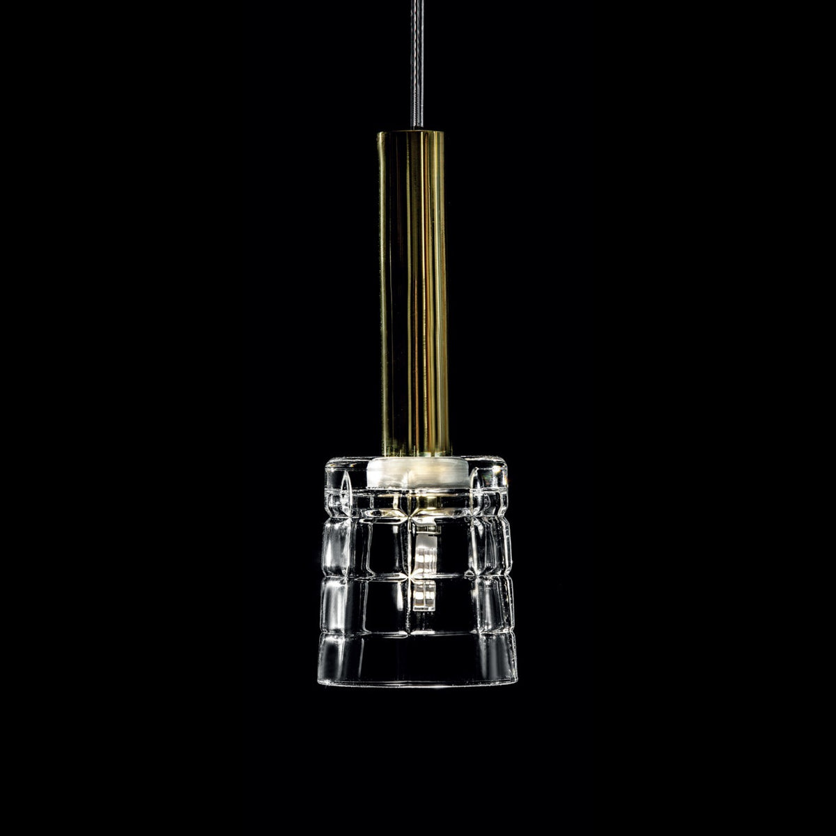 Détail rapproché d'un luminaire suspendu, verre transparent quadrillé et douille dorée éclairée.