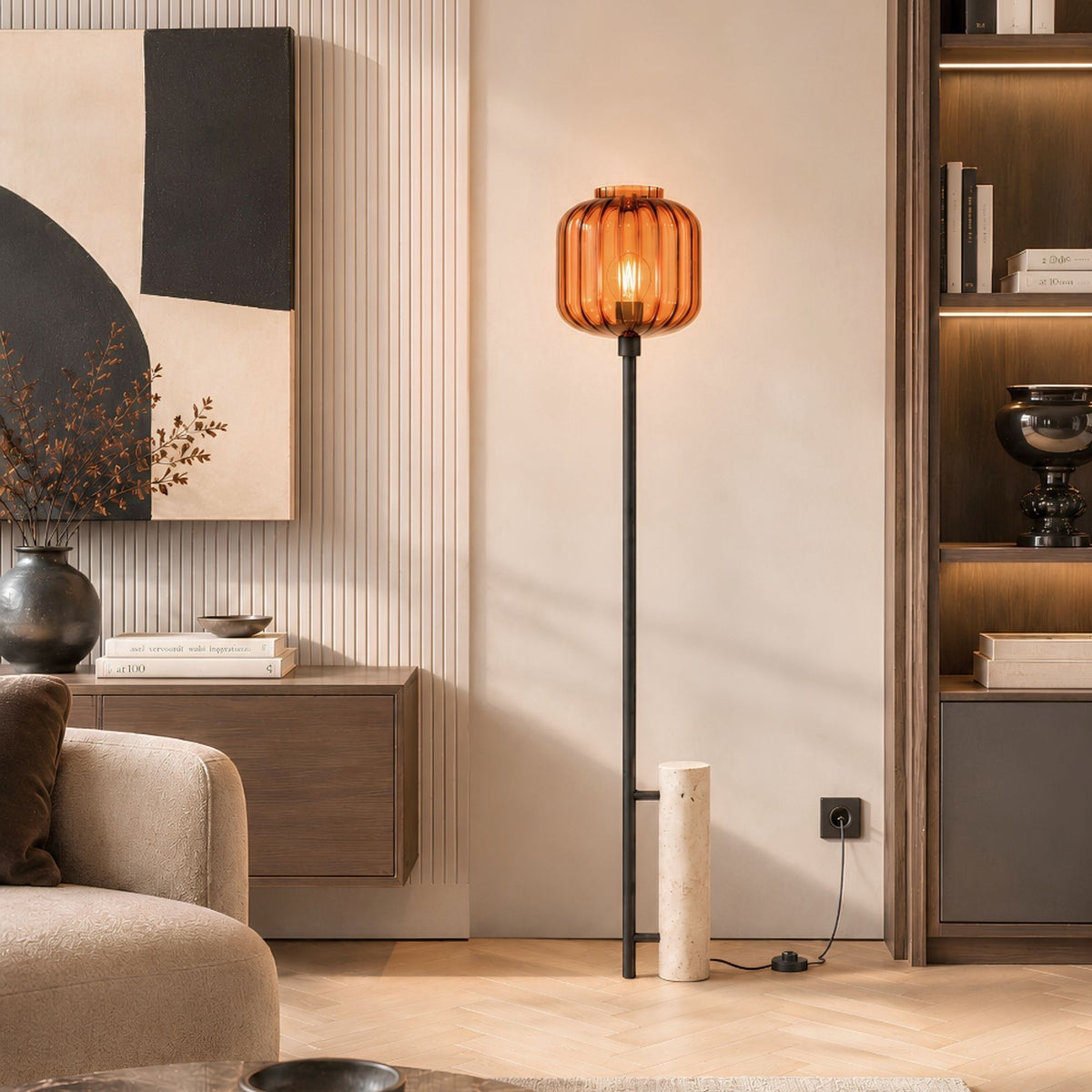 Lampadaire à verre ambré devant un mur clair, parquet en chevrons et bibliothèque