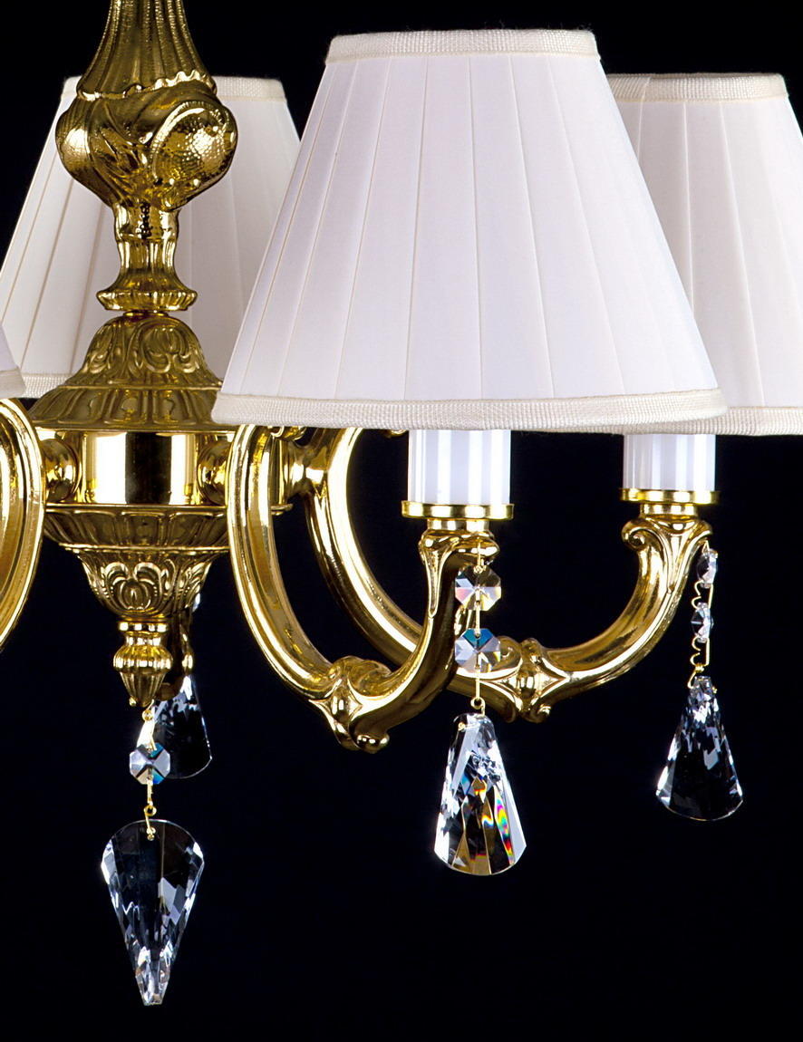 Détail des bras dorés recourbés, abat-jours plissés et gouttes de cristal