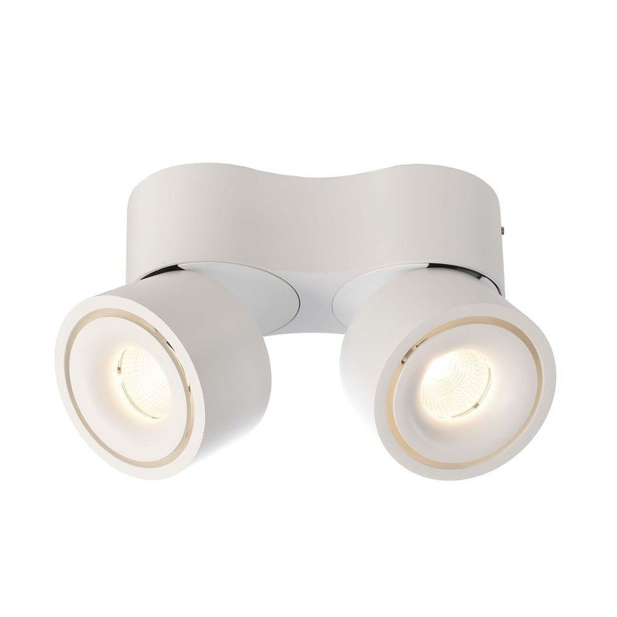 Spot double blanc fixé au plafond, deux têtes rondes orientables allumées, vue de face.