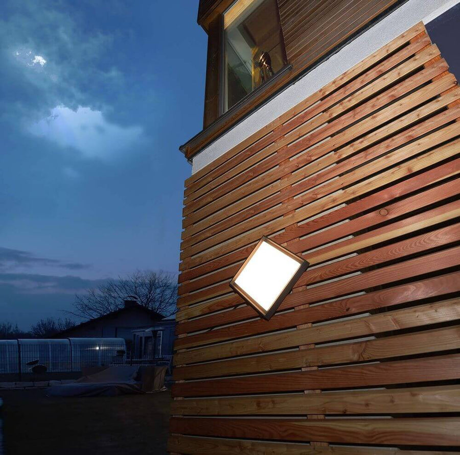 Luminaire carré allumé fixé sur une façade extérieure en lattes de bois au crépuscule.