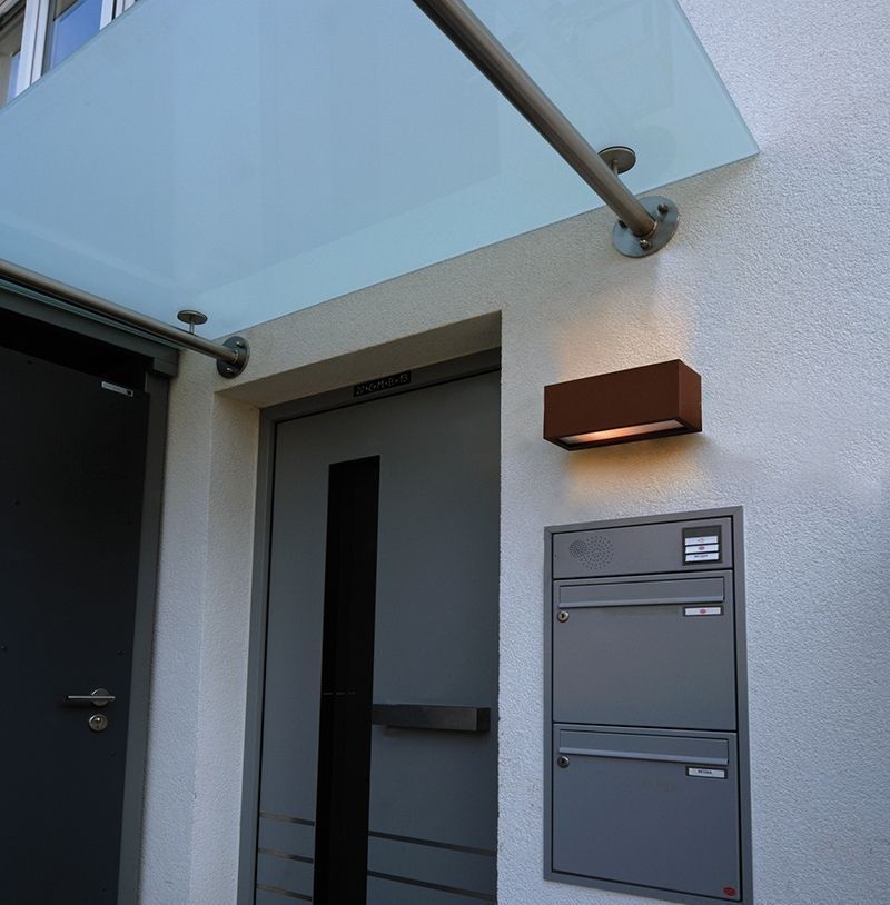 Applique marron fixée sur mur extérieur clair, au-dessus d'une boîte aux lettres