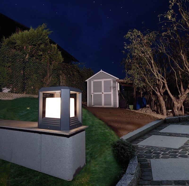 Mise en ambiance nocturne : lanterne allumée posée sur un muret de jardin.