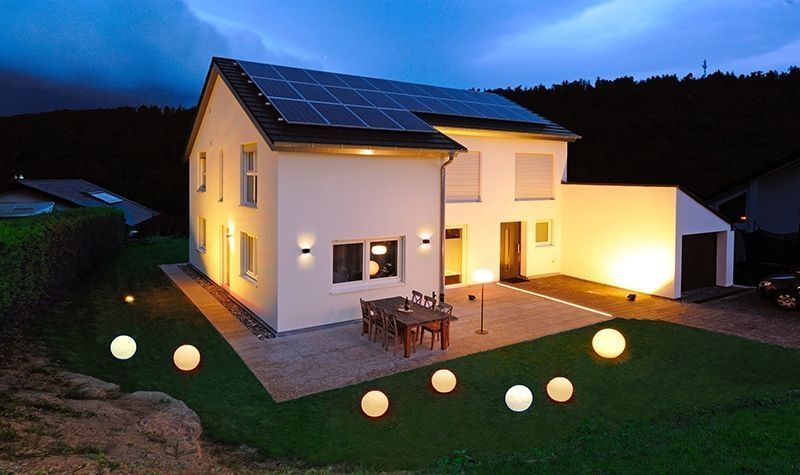 Maison au crépuscule avec plusieurs sphères lumineuses posées sur la pelouse et la terrasse.