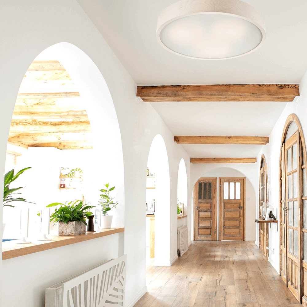 Mise en ambiance dans un couloir blanc aux arches et poutres en bois.