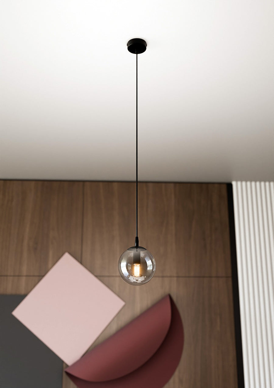 Suspension globe en verre fumé suspendue au-dessus d'une table en bois avec papiers colorés.