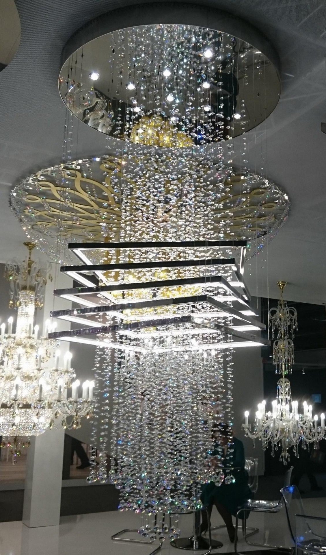 Présentation en showroom d'un grand lustre à pampilles et cadres carrés, avec d'autres luminaires.