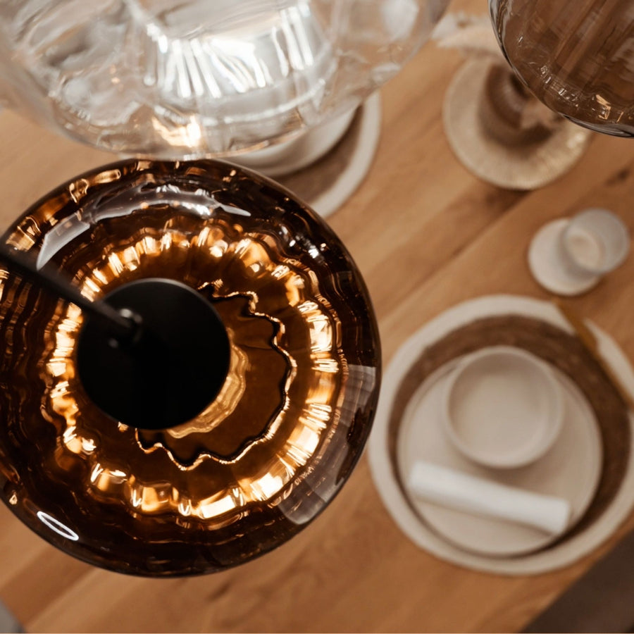 Vue du dessus d'une suspension en verre ambré au-dessus d'une table dressée avec assiettes.