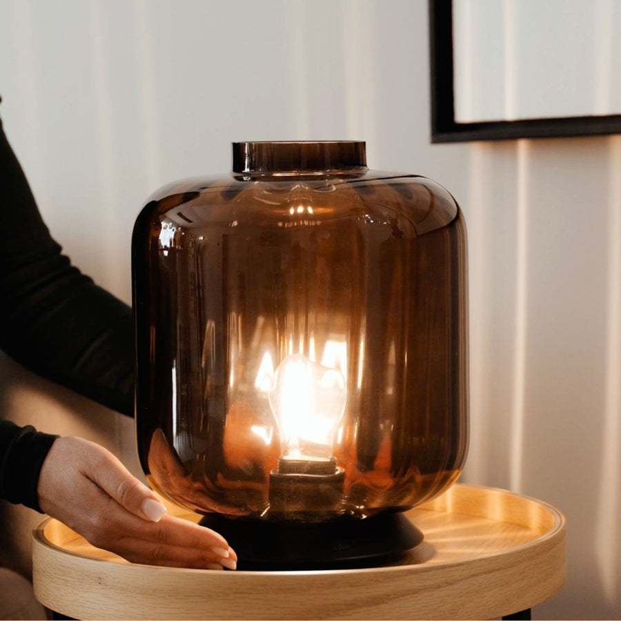 Détail de la finition : main posée près du socle noir, reflets chauds sur le verre fumé