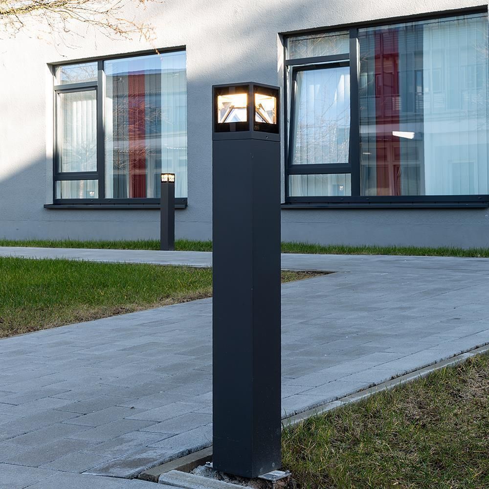 Borne anthracite photographiée de jour sur une allée pavée devant un bâtiment moderne