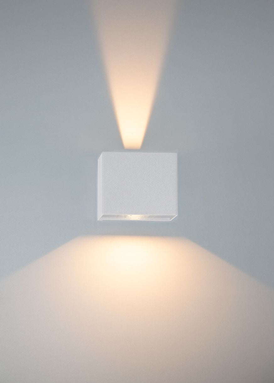 Détail d'une applique blanche projetant deux faisceaux lumineux verticaux sur le mur.