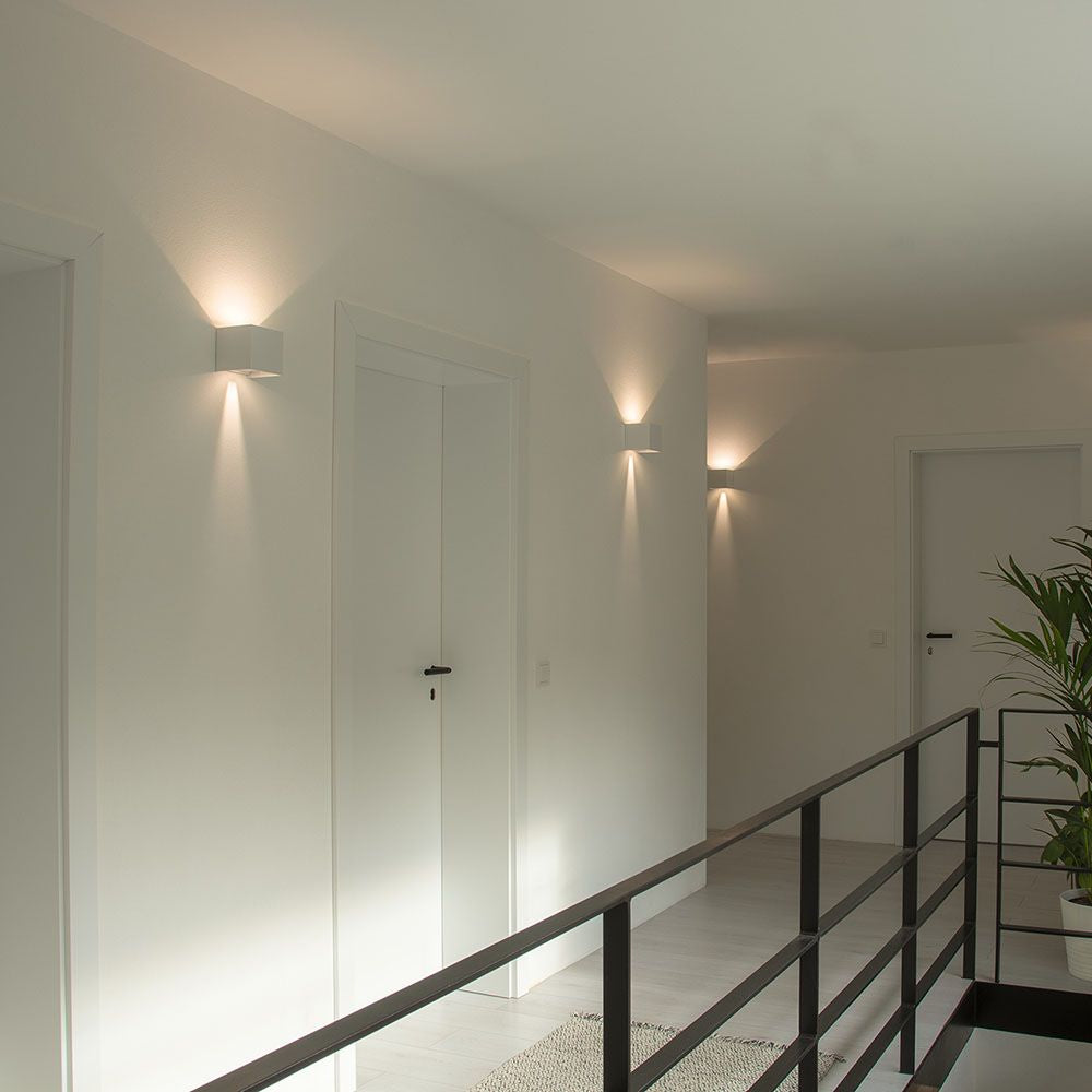Couloir blanc avec plusieurs appliques murales allumées au-dessus des portes.