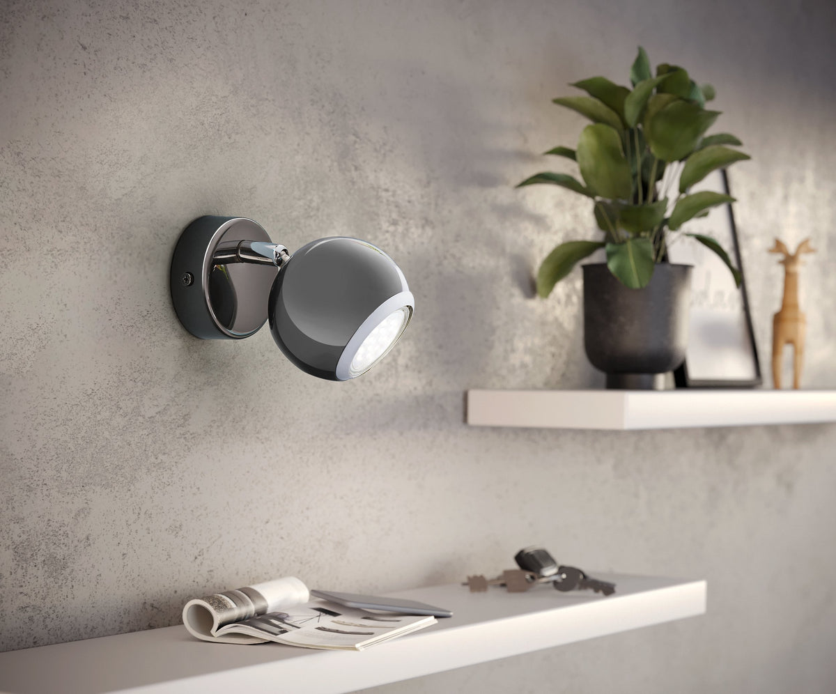 Mise en ambiance de l applique allumée sur un mur gris près d une étagère