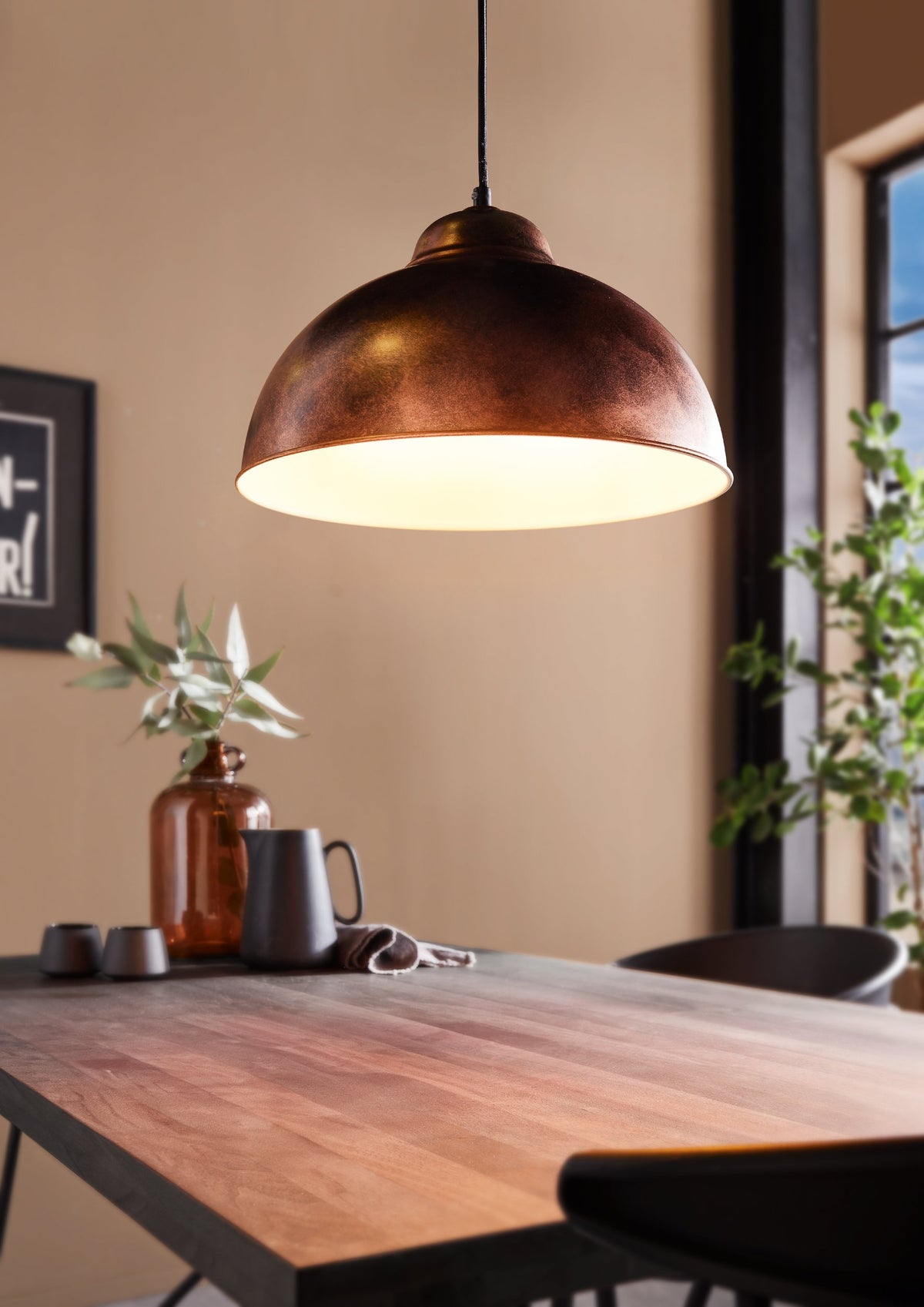 Mise en ambiance au-dessus d'une table en bois, suspension allumée éclairant la pièce.