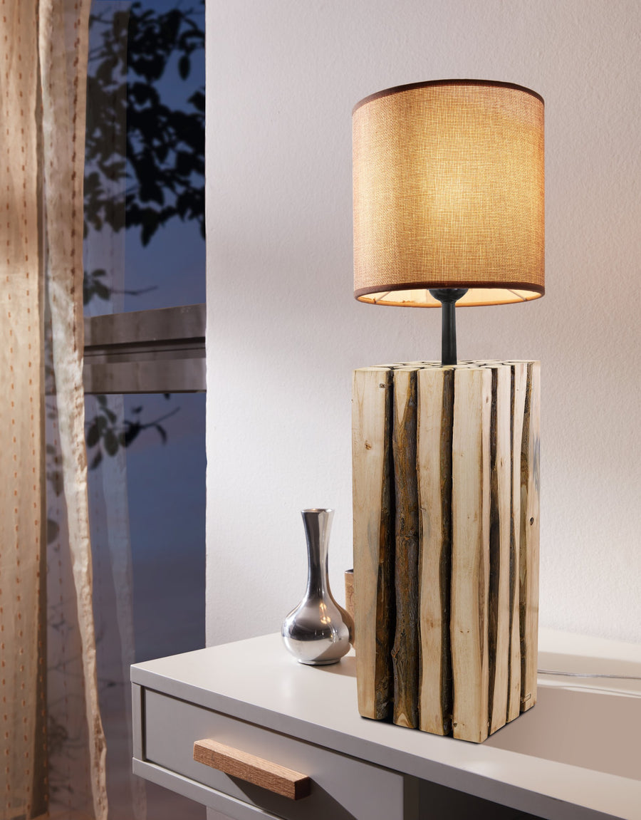 Lampe à poser allumée avec abat-jour cylindrique beige, posée sur une commode blanche.