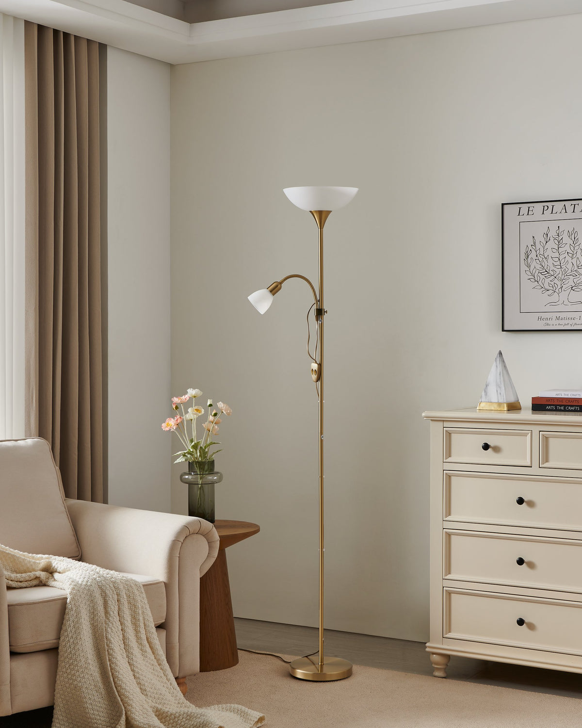 Mise en ambiance dans un salon beige, lampadaire allumé près d'un fauteuil et d'une commode.