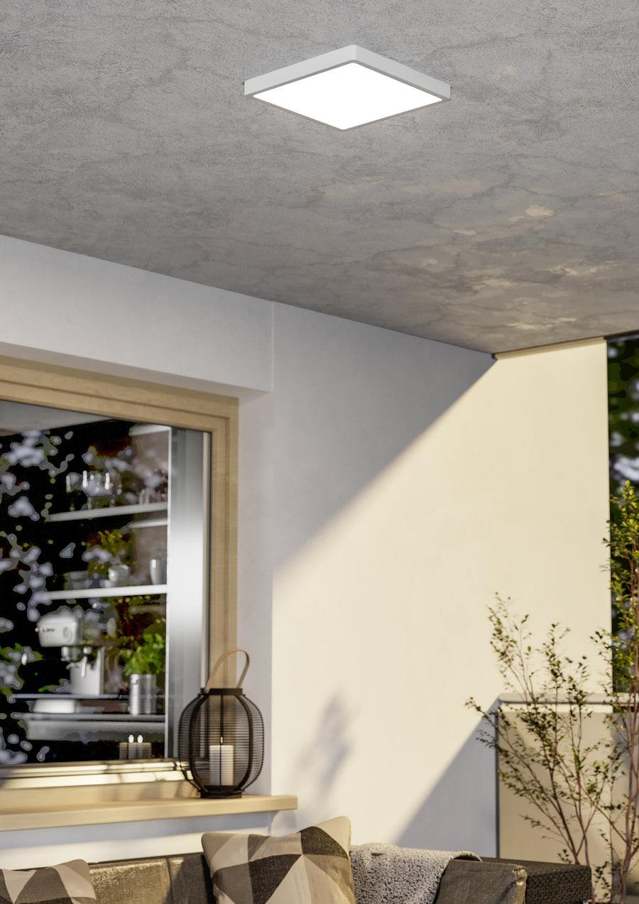 Luminaire carré blanc fixé au plafond d'une terrasse couverte, éclairant un mur extérieur.