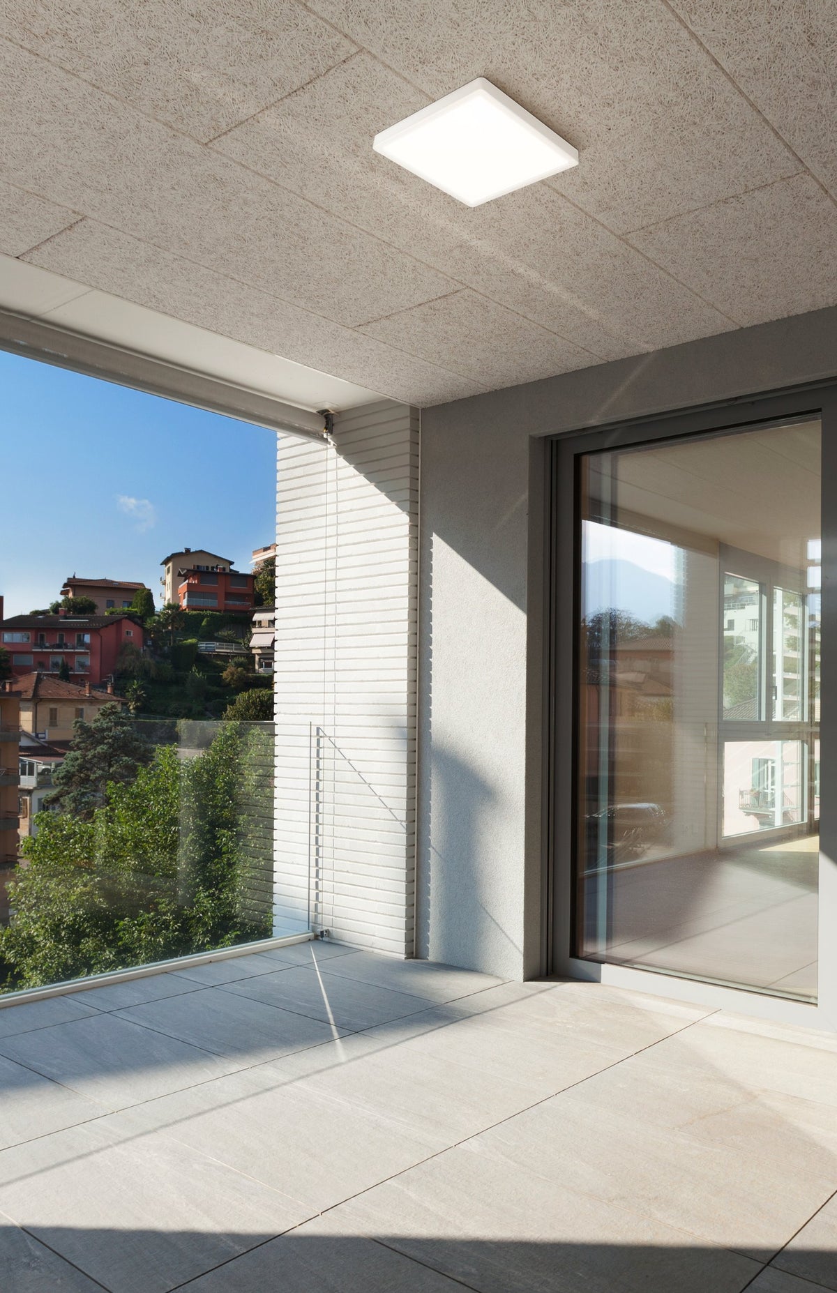 Luminaire carré blanc allumé au plafond d'un balcon avec vue sur les collines.