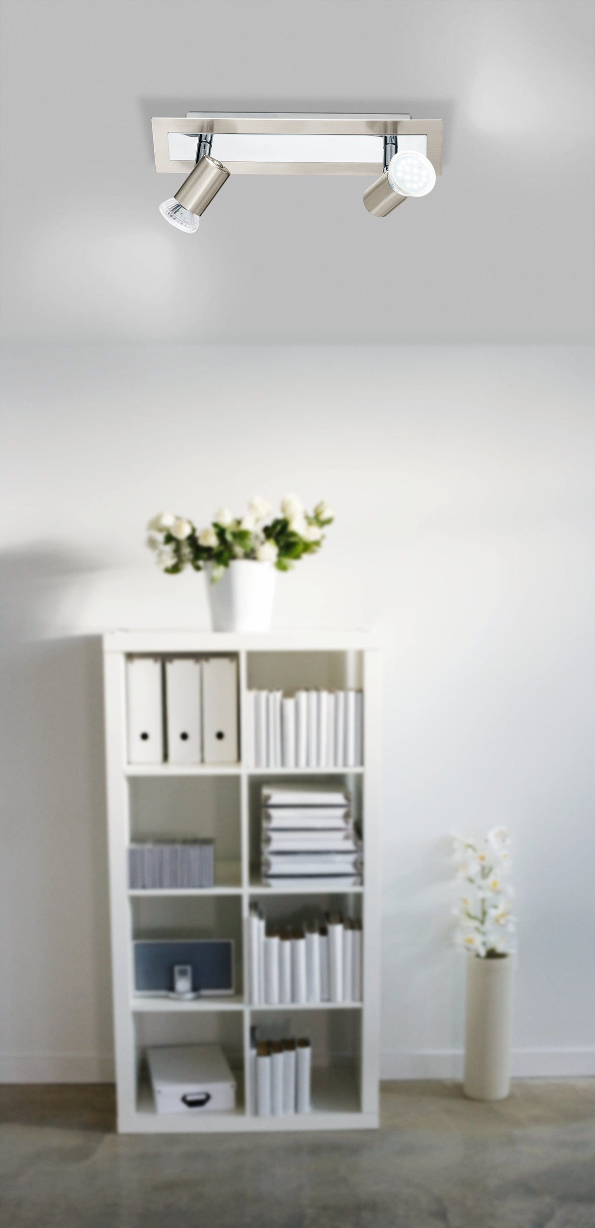 Mise en ambiance du spot plafond dans un salon blanc avec bibliothèque et fleurs.