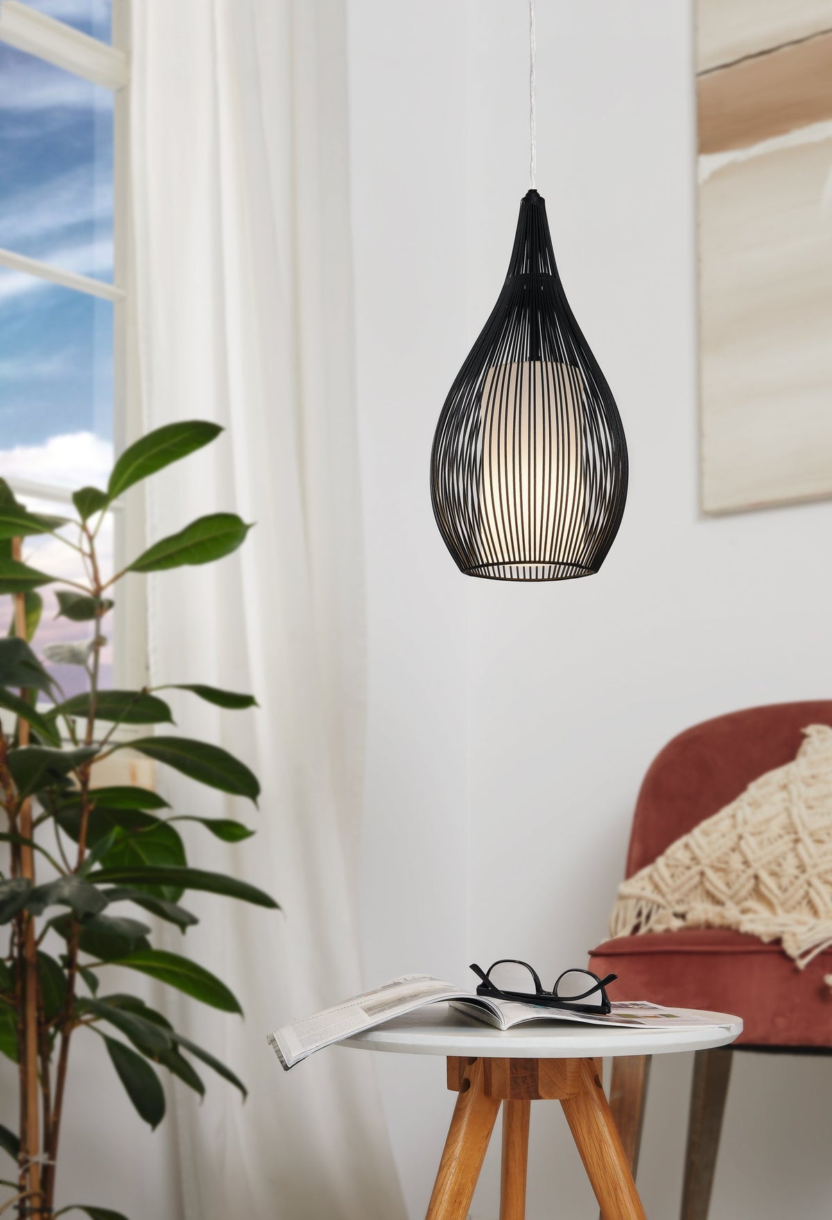 Mise en ambiance : suspension allumée au-dessus d'une table, plante et fauteuil.