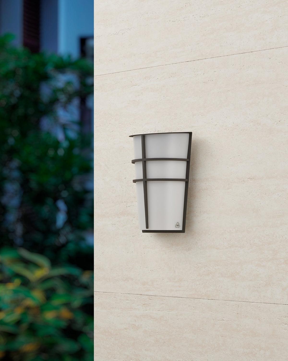 Même applique éteinte fixée sur mur clair, feuillage sombre flou en arrière-plan