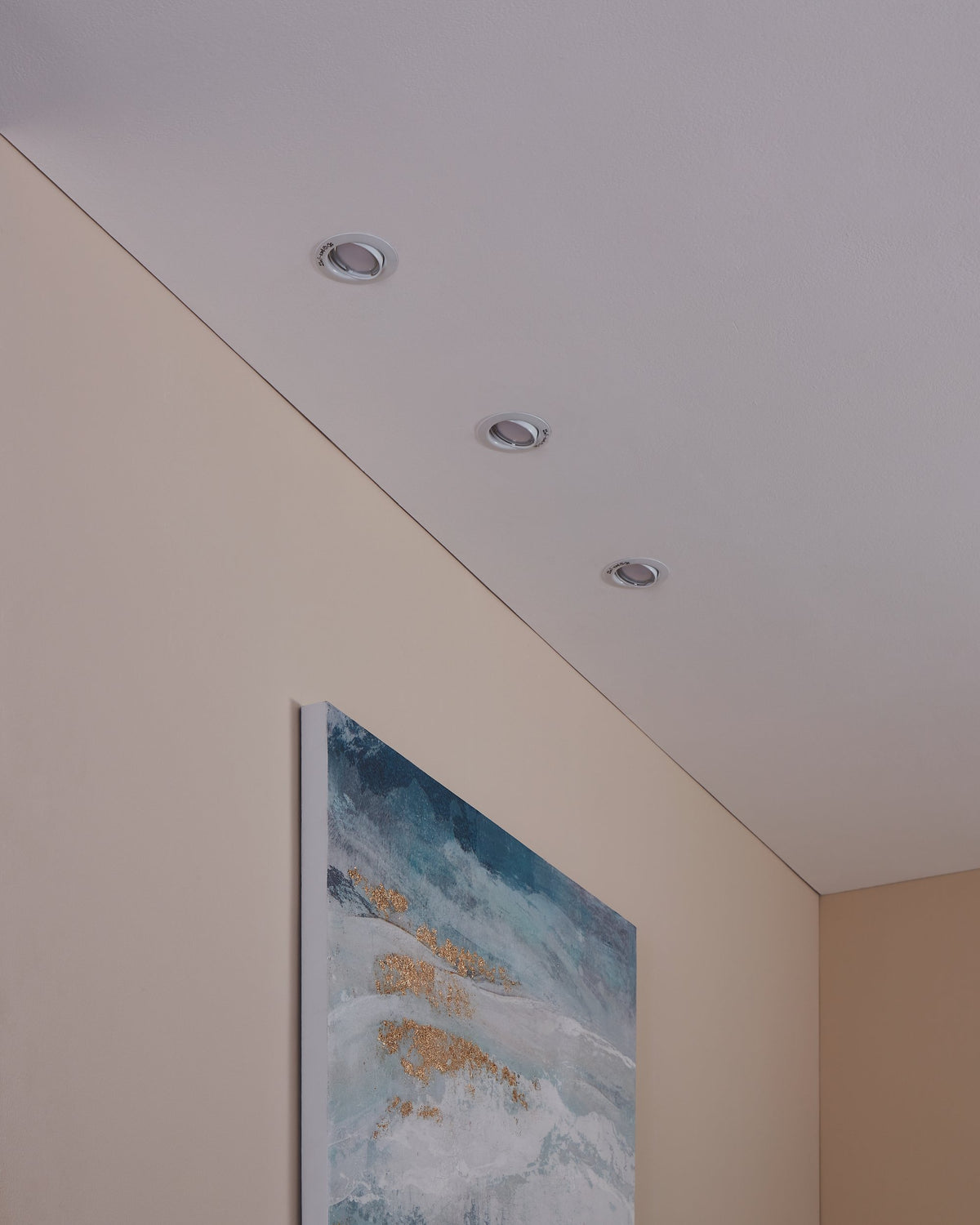 Vue en plongée de trois spots encastrés éteints au plafond, près d'un tableau