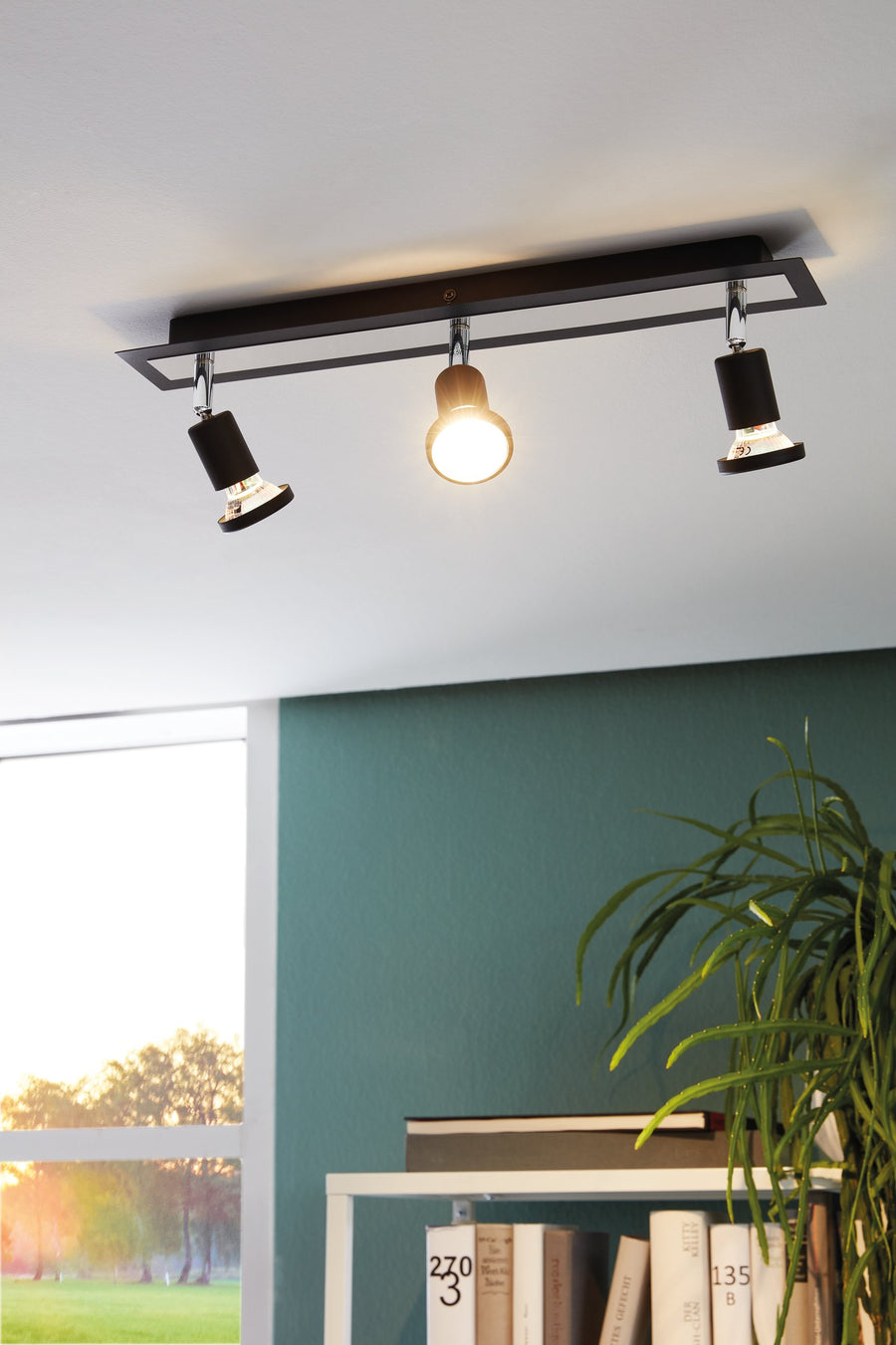 Spot allumé fixé au plafond au-dessus d'un mur vert et d'une plante