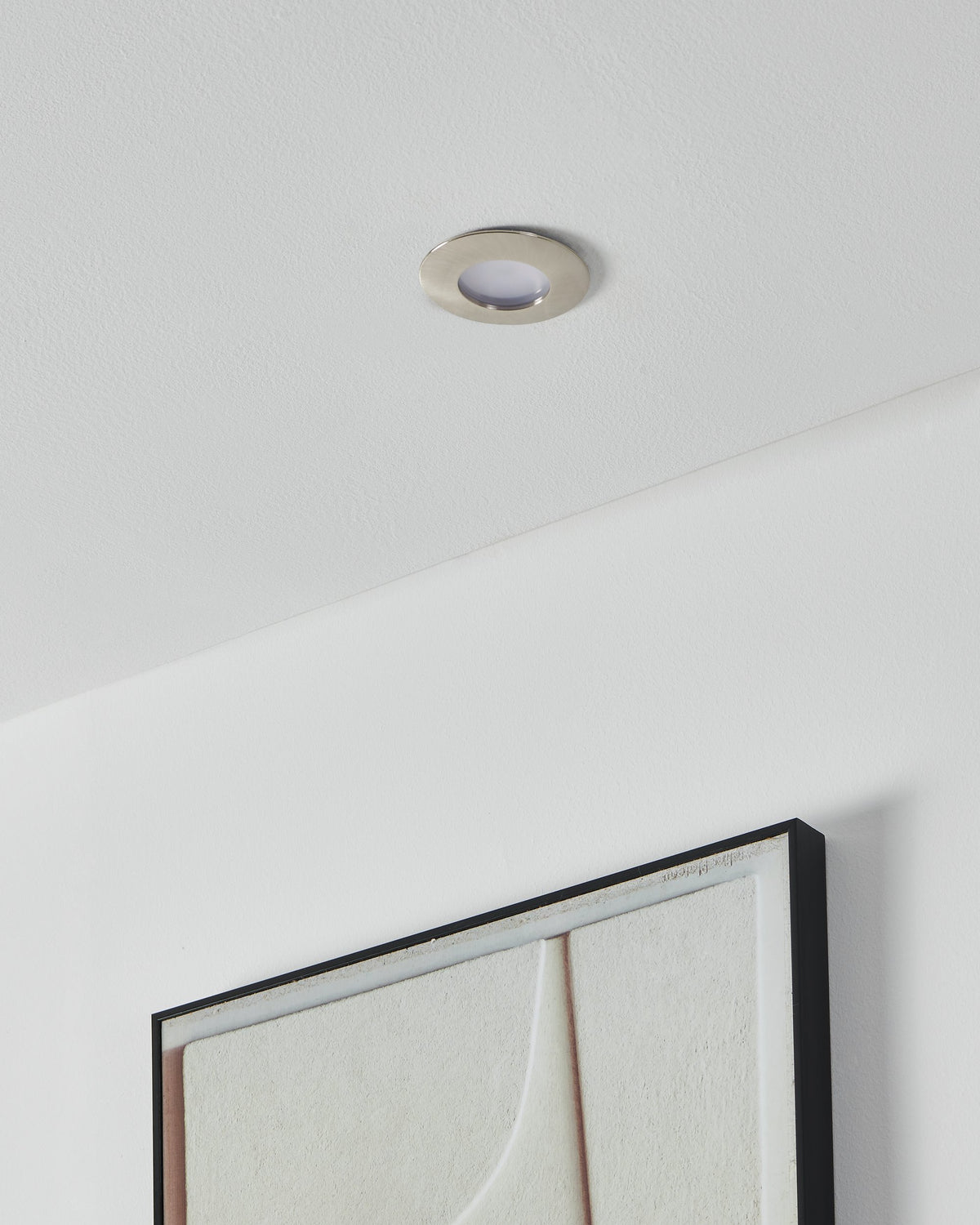 Spot encastré éteint au plafond blanc, au-dessus d'un tableau encadré