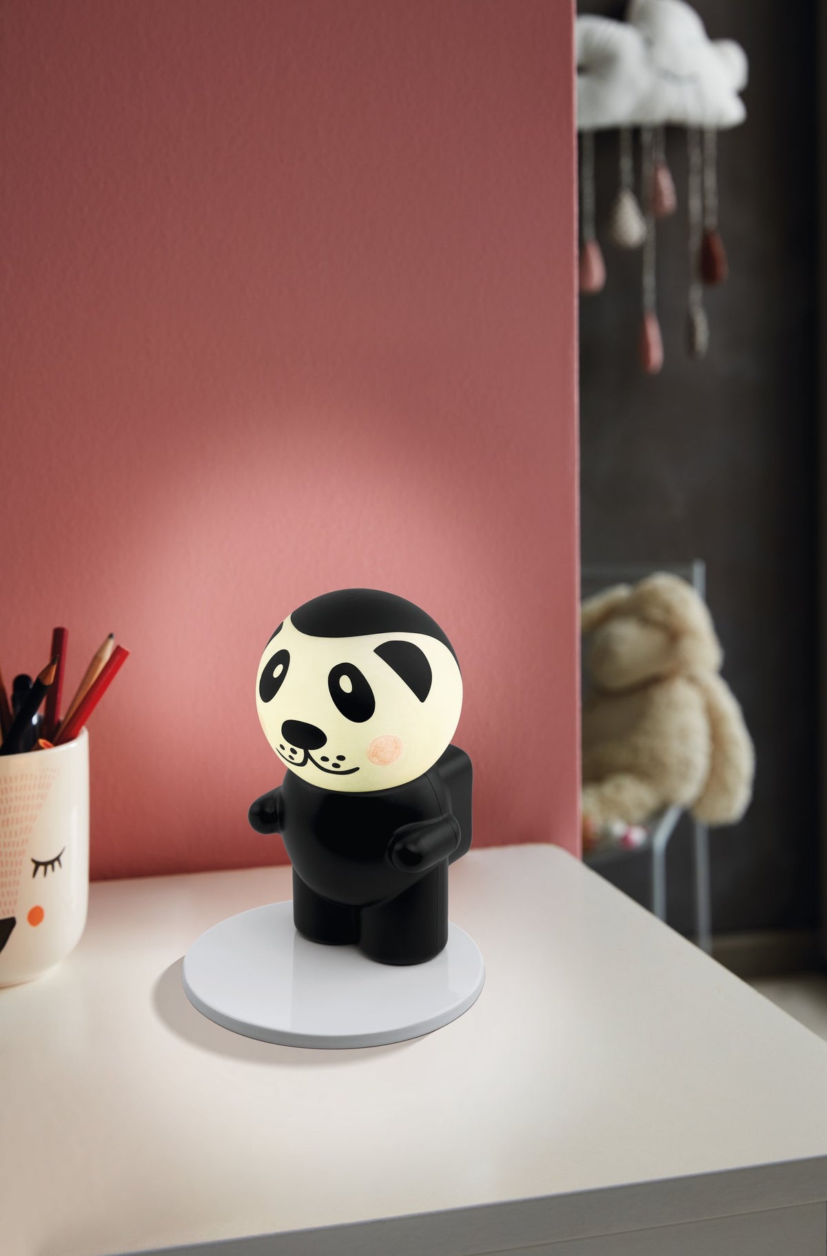 Lampe panda allumée sur un bureau, mur rose et peluches en arrière-plan flou